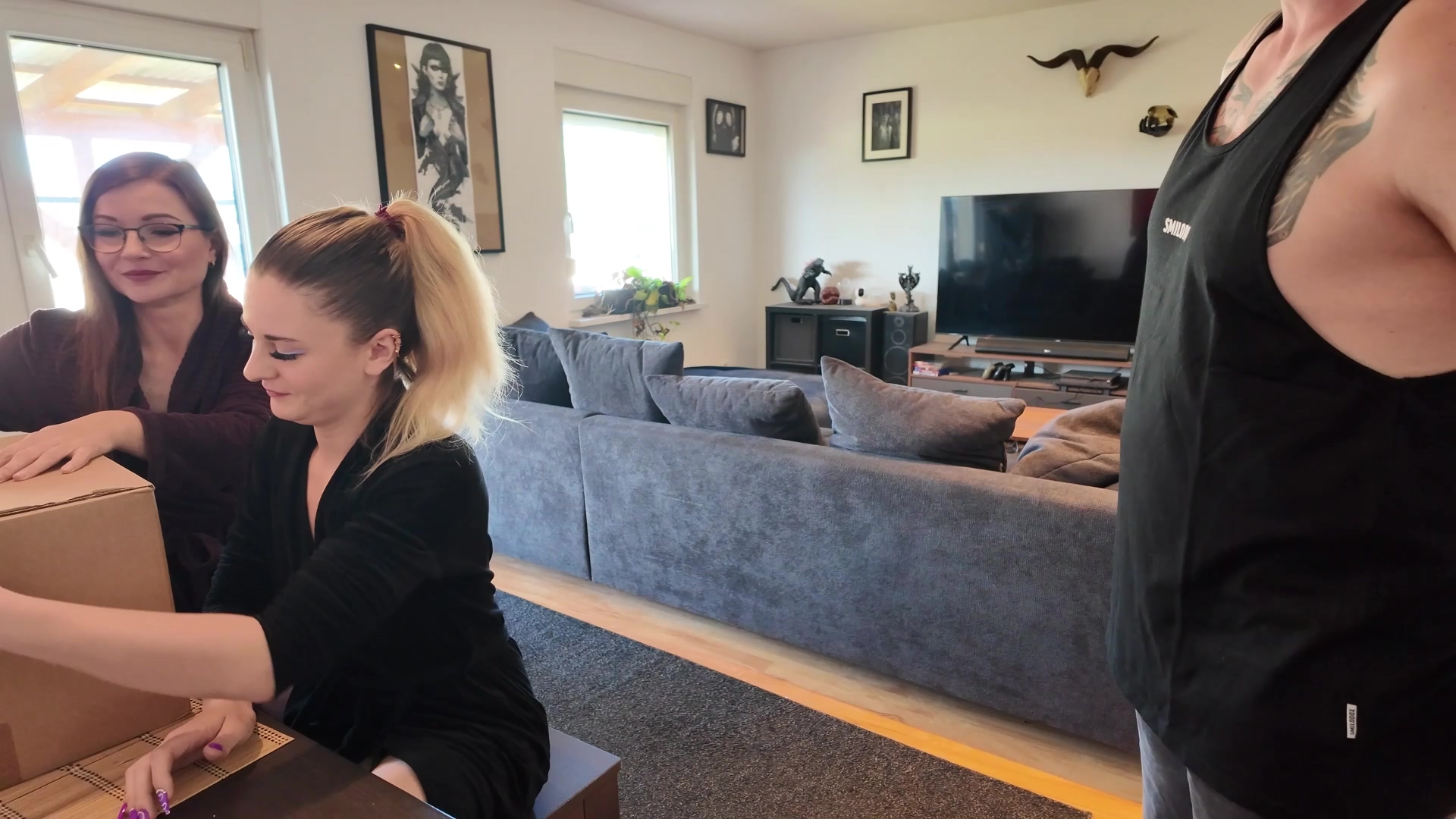 Melly und Emily hatten diesen seltenen Nachmittag, an dem Zeit weich wird. Beide saßen am Küchentisch, Kaffee dampfte, Gespräche schlenderten ohne Ziel. Die Fenster standen offen, Sommerluft lag im Raum, dazu ein Hauch von Langeweile – die gute Sorte, aus der Ideen entstehen. Dann klingelte es. Nicht hastig, nicht schüchtern, sondern selbstbewusst. Emily hob eine Braue und sah Melly an, die nur den Kopf schüttelte und zur Tür ging. Draußen stand der Postbote, groß und entspannt, mit einem mühelosen Lächeln. Das Shirt saß ein wenig zu gut, der Blick war wach. Unter dem Arm trug er ein schlichtes Paket mit dunklem Aufkleber. Sonderlieferung, sagte er ruhig. Melly nahm es entgegen, ihre Finger berührten sich einen Moment zu lang. Emily lehnte im Hintergrund am Türrahmen und beobachtete alles mit offener Neugier. Ein kurzer Moment Stille folgte, kein unangenehmer, sondern einer voller Möglichkeiten. Dann verabschiedete sich der Postbote langsam. Die Tür schloss sich. Melly